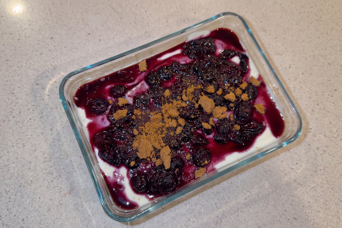 Overnight blueberry cheesecake in a glass dish, topped with blueberry compote and biscuit crumb